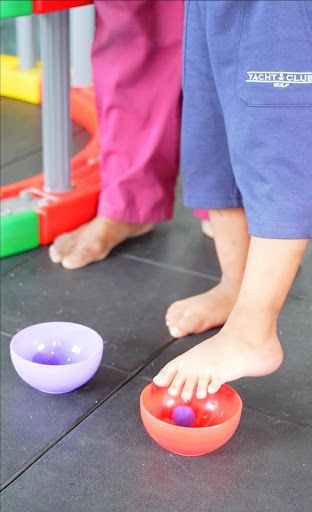 Children using their bare feet to explore colorful sensory bowls during a play activity.